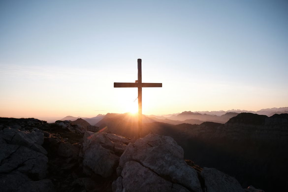 A wooden cross at sunrise on a mountain summit